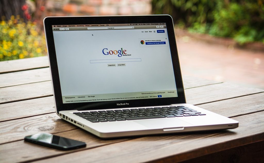 MacBook on a wooden table open with Google and a phone